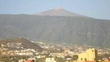 Una muntanya amb un pic vermell, envoltada per una població amb edificis i un cel serè.