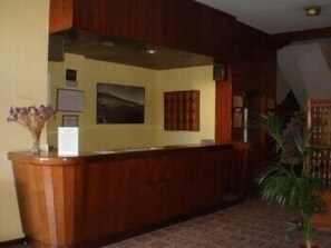 Un mostrador de recepción con detalles de madera, un cuadro enmarcado en la pared y una pequeña planta en maceta a la izquierda.