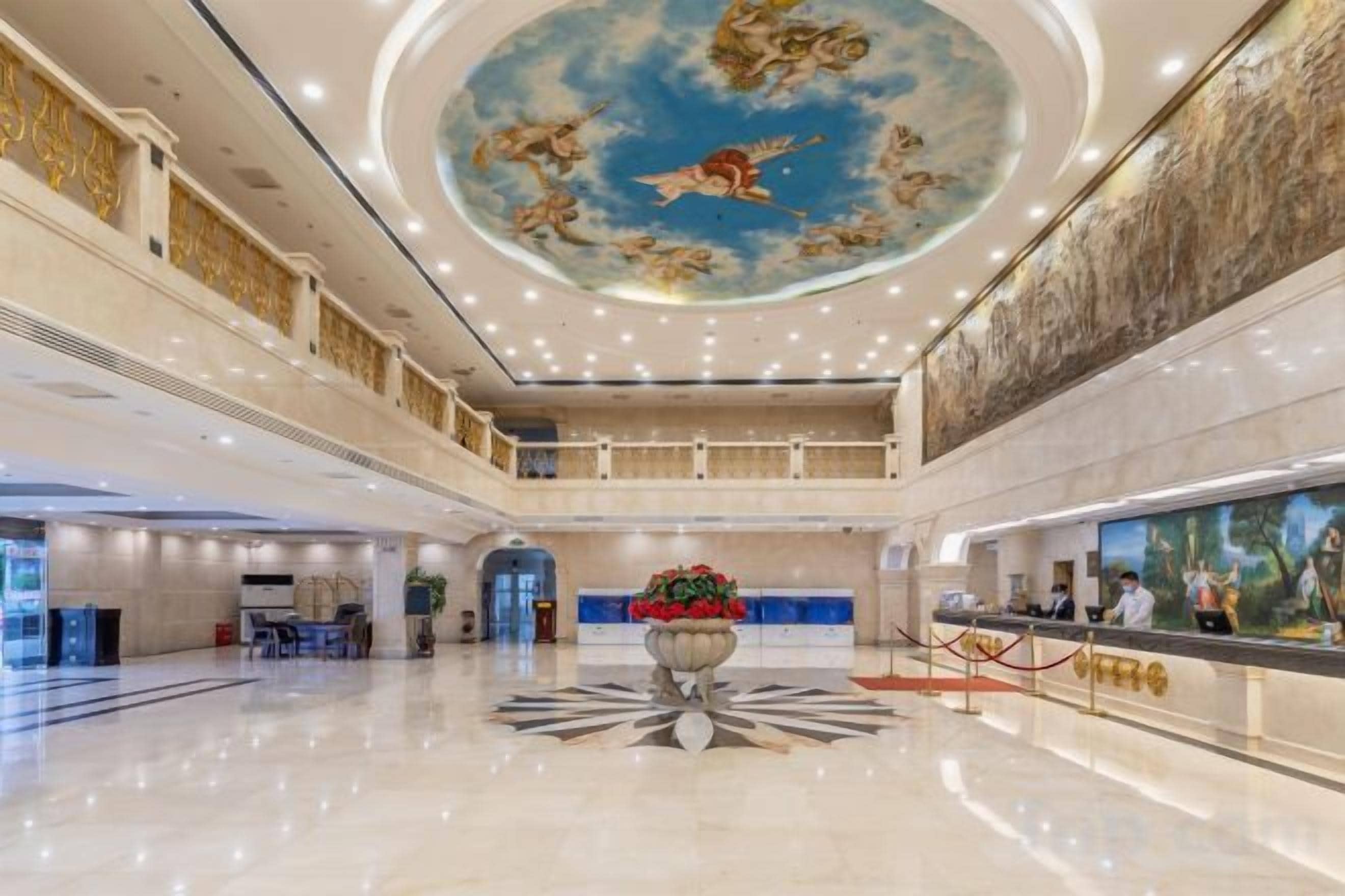 A spacious lobby with a high ceiling, a central floral arrangement, and a reception desk.