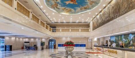 A spacious lobby with a high ceiling, a central floral arrangement, and a reception desk.