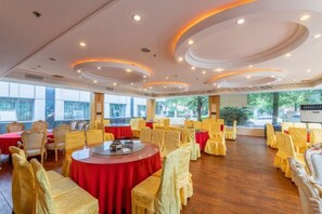 Une salle de banquet avec des tables rondes, des chaises jaunes et des nappes rouges.
