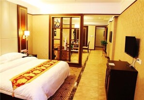 A hotel room with a large bed, a desk with a television, a mirror, and a sliding door leading to a dining area. - zhangjiajie Lantian Hotel (Zhangjiajie)