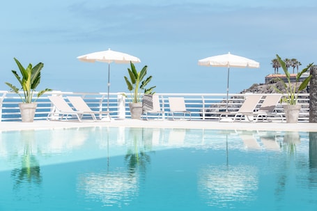 Una piscina al aire libre, sombrillas, sillones reclinables de piscina