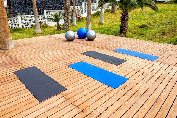 Una terraza de madera con colchonetas de ejercicio y tres pelotas de gimnasia.