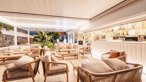 A spacious outdoor lounge area with wicker furniture, a bar, and a stone wall backdrop. - Atlantic Holiday Hotel (Adeje)