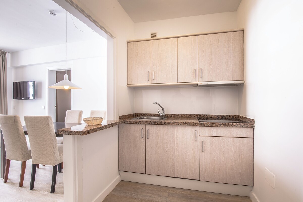A modern kitchen with light wood cabinets, a granite countertop, and a built-in sink.
