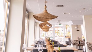 A restaurant interior with large woven pendant lights, wooden tables, and a view of the city through large windows. - Atlantic Holiday Hotel (Adeje)