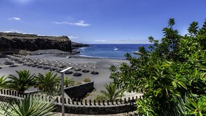 A beach with umbrellas and lounge chairs, a rocky cliff, and a clear blue sky. - Atlantic Holiday Hotel (Adeje)