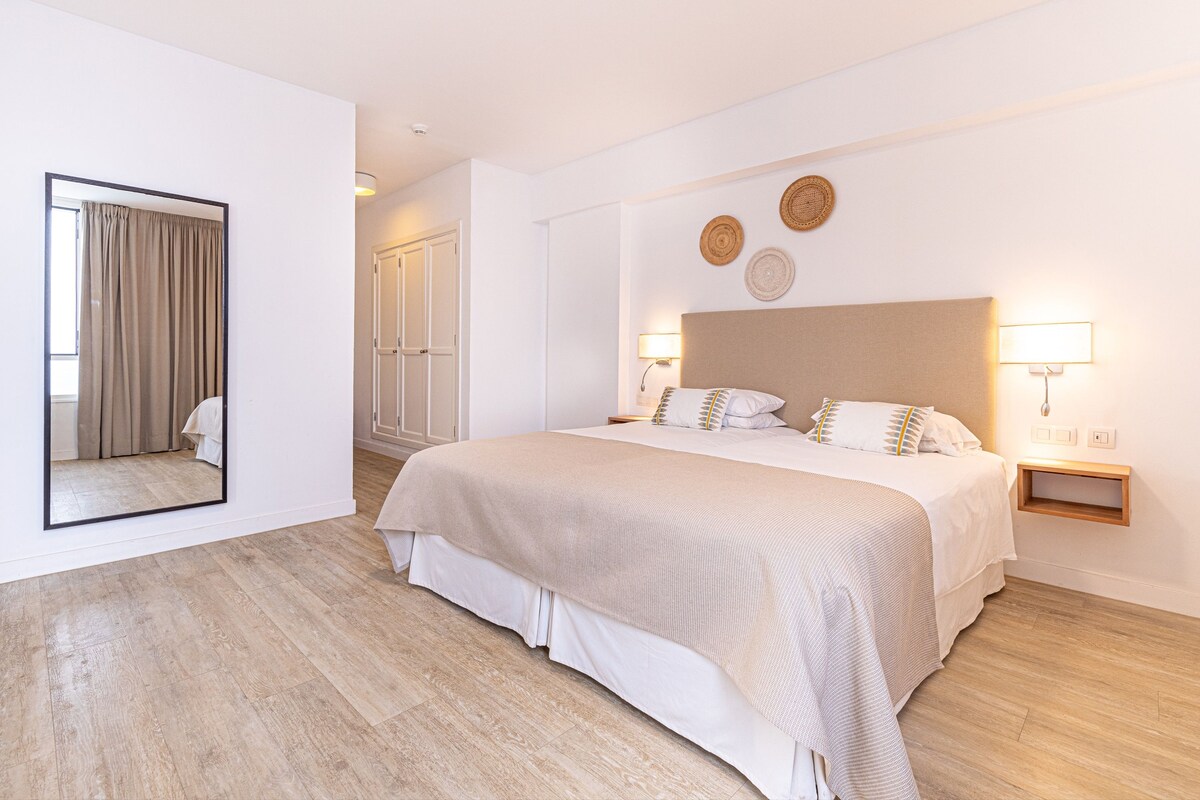 A modern hotel room with a large bed, bedside lamps, a mirror, and a view of the bathroom.
