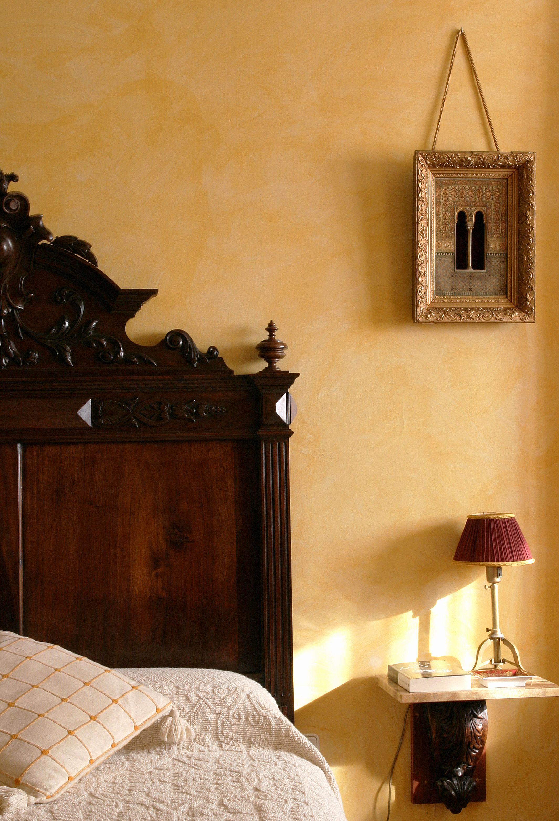 A bedroom with a wooden headboard, a bedside table with a lamp, and a framed picture on the wall.