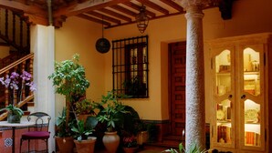 Un patio con baldosas de terracota, plantas en macetas, una silla de madera, una escalera y una puerta con paneles de vidrio.