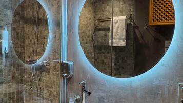 A bathroom with a marble sink, two round mirrors, a shower, and a towel rack.
