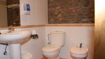 A bathroom with a sink, two toilets, and a stone wall.