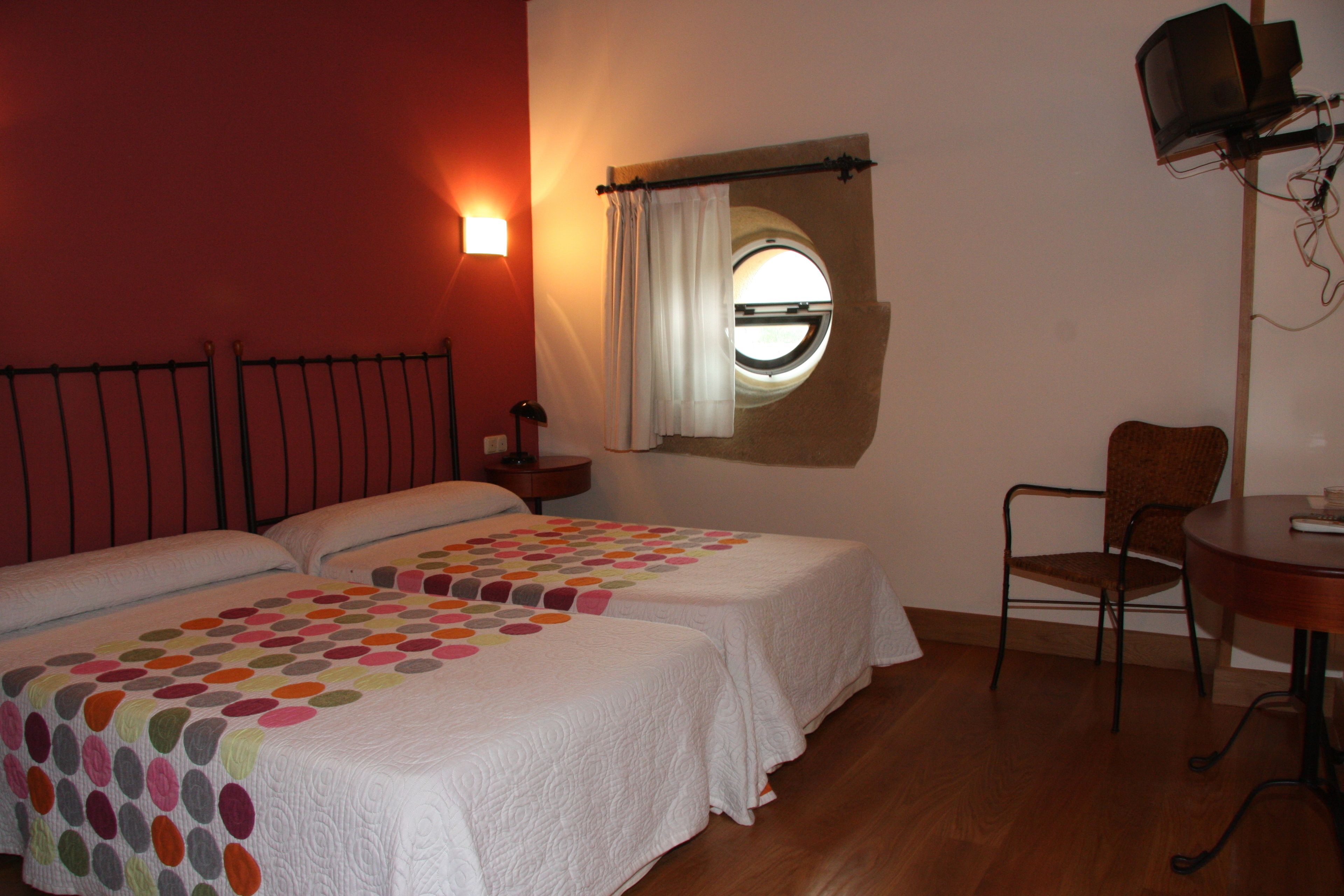 A room with two beds, a round window, a chair, and a table.