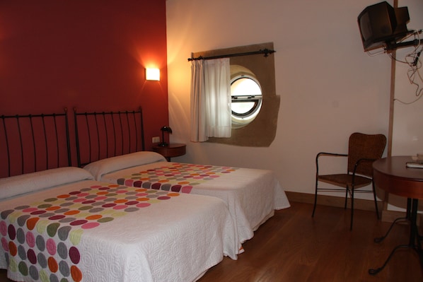A room with two beds, a round window, a chair, and a table. - Hotel Palacio Atxega (Usurbil)