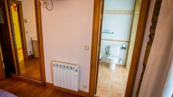 A room with a wooden floor, a radiator, a television mounted on the wall, and a bathroom visible through an open door.