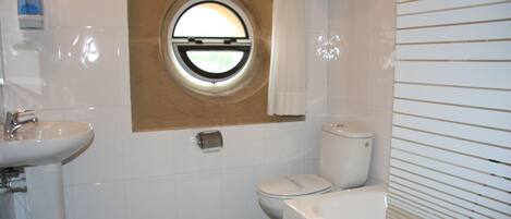 A bathroom with a round window, a sink, toilet, and bathtub.
