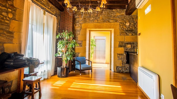 A cozy room with stone walls, a wooden ceiling, a chandelier, a potted plant, a blue chair, and a radiator. - Hotel Palacio Atxega (Usurbil)