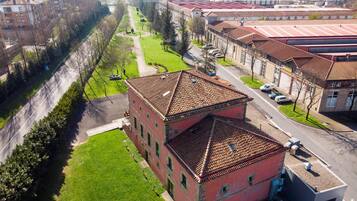 A red brick building with a tiled roof, surrounded by a green lawn and a paved road.