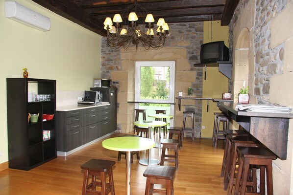 A kitchen with a stone wall, wooden bar, and a round table with stools. - Hotel Palacio Atxega (Usurbil)