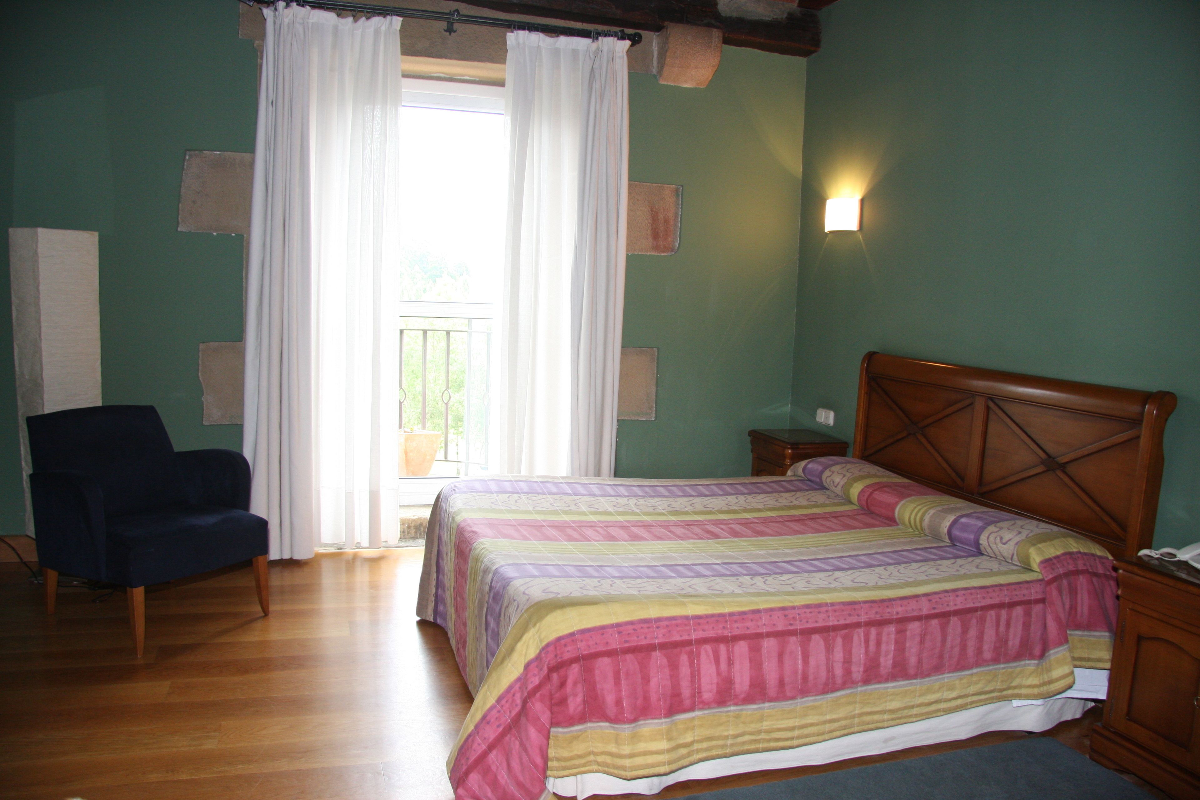 A bedroom with a bed, a chair, a nightstand, and a window with curtains.
