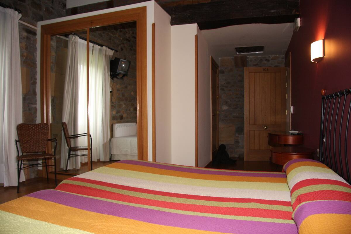 A hotel room with a large bed, a wooden door, a stone wall, and a chair.