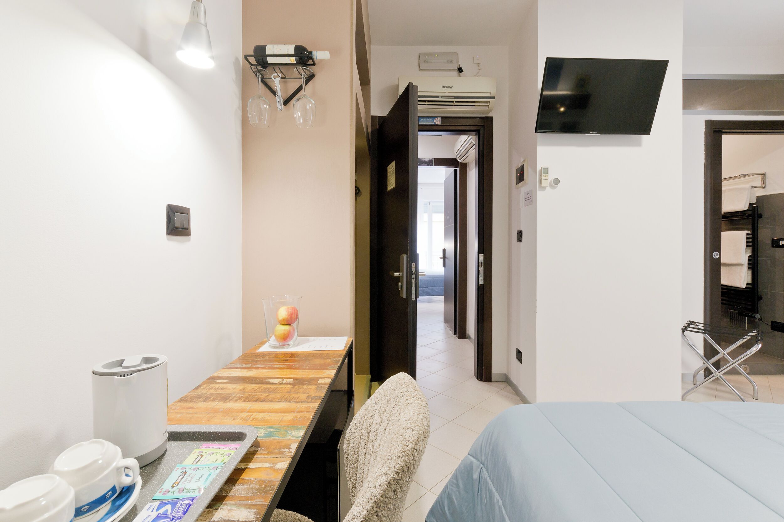 Una habitación de hotel con una cama, un escritorio con una silla, un televisor montado en la pared y un baño visible a través de una puerta abierta.