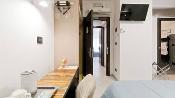 Una habitación de hotel con una cama, un escritorio con una silla, un televisor montado en la pared y un baño visible a través de una puerta abierta.