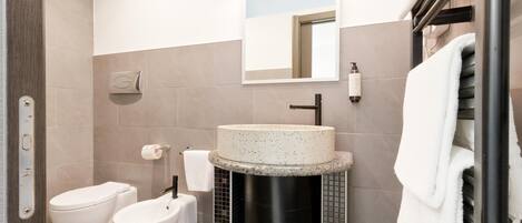 Un baño moderno con un lavabo redondo, un inodoro y un bidé.