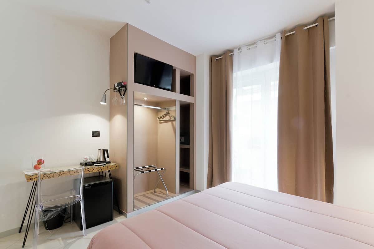 A bedroom with a bed, a desk with a computer, a small fridge, and a closet with a hanging rack.
