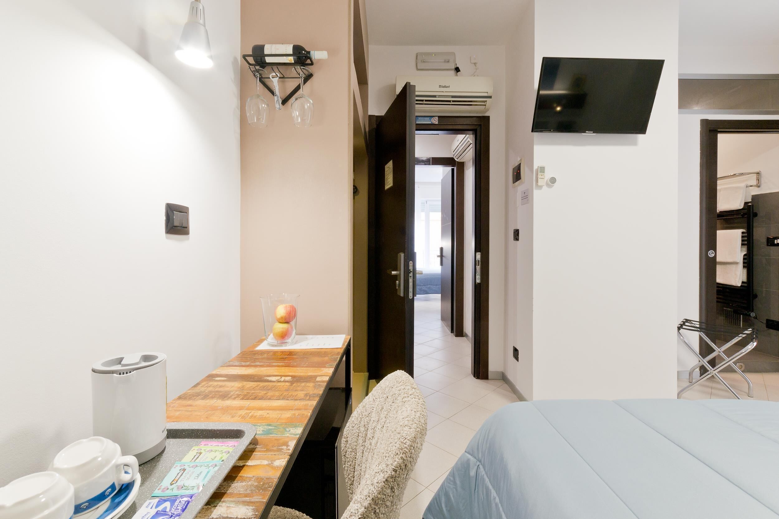 Hotelkamer met een bed, een bureau met stoel, een koffieapparaat, een televisie en een badkamer zichtbaar door een geopende deur.