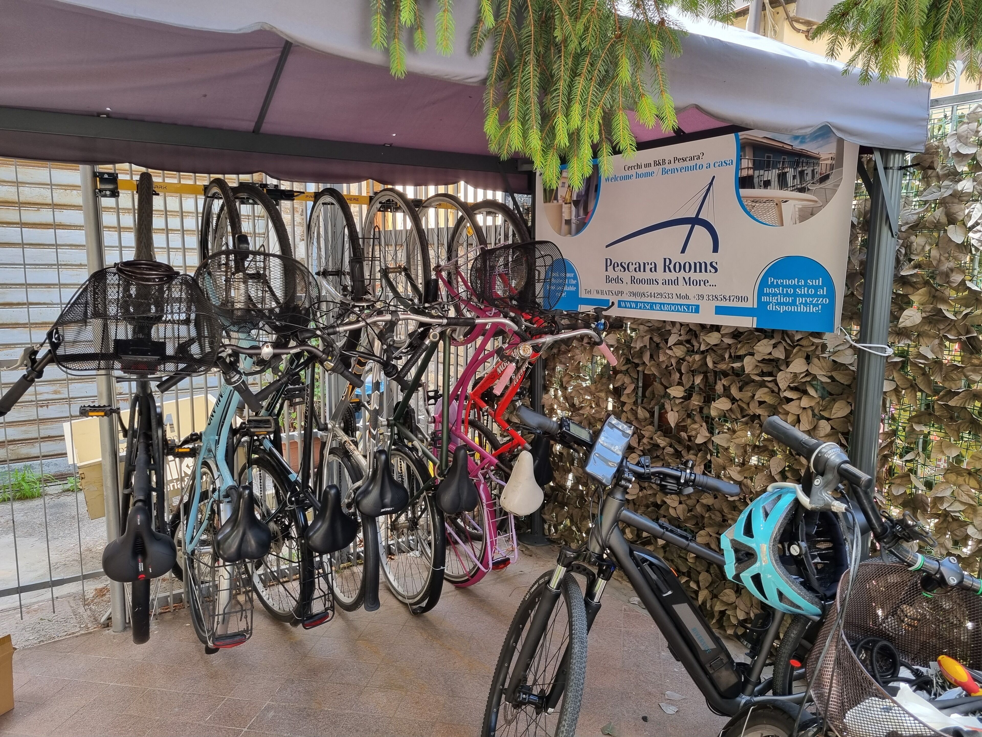 Un punto noleggio biciclette con diverse bici e un cartello pubblicitario per Pescara Rooms.