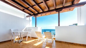 A balcony with a wooden ceiling, white chairs, a table, and a view of the ocean. - Apartamentos Albatros (Adeje)
