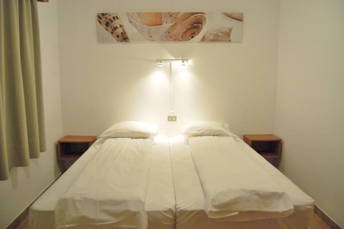 A double bed with white linens, two bedside tables, a wall-mounted light fixture, and a partial view of a poster above the bed.