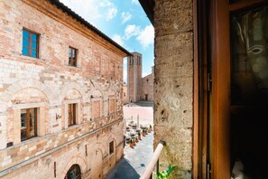 Una calle estrecha con un edificio que presenta ventanas arqueadas y una torre de campanas. Hay mesas y sillas al aire libre a lo largo de la calle.