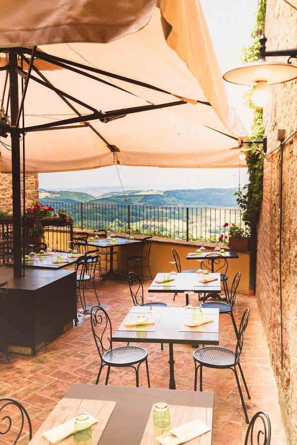 Une terrasse extérieure avec des tables et des chaises, un grand parasol et une vue sur la campagne.