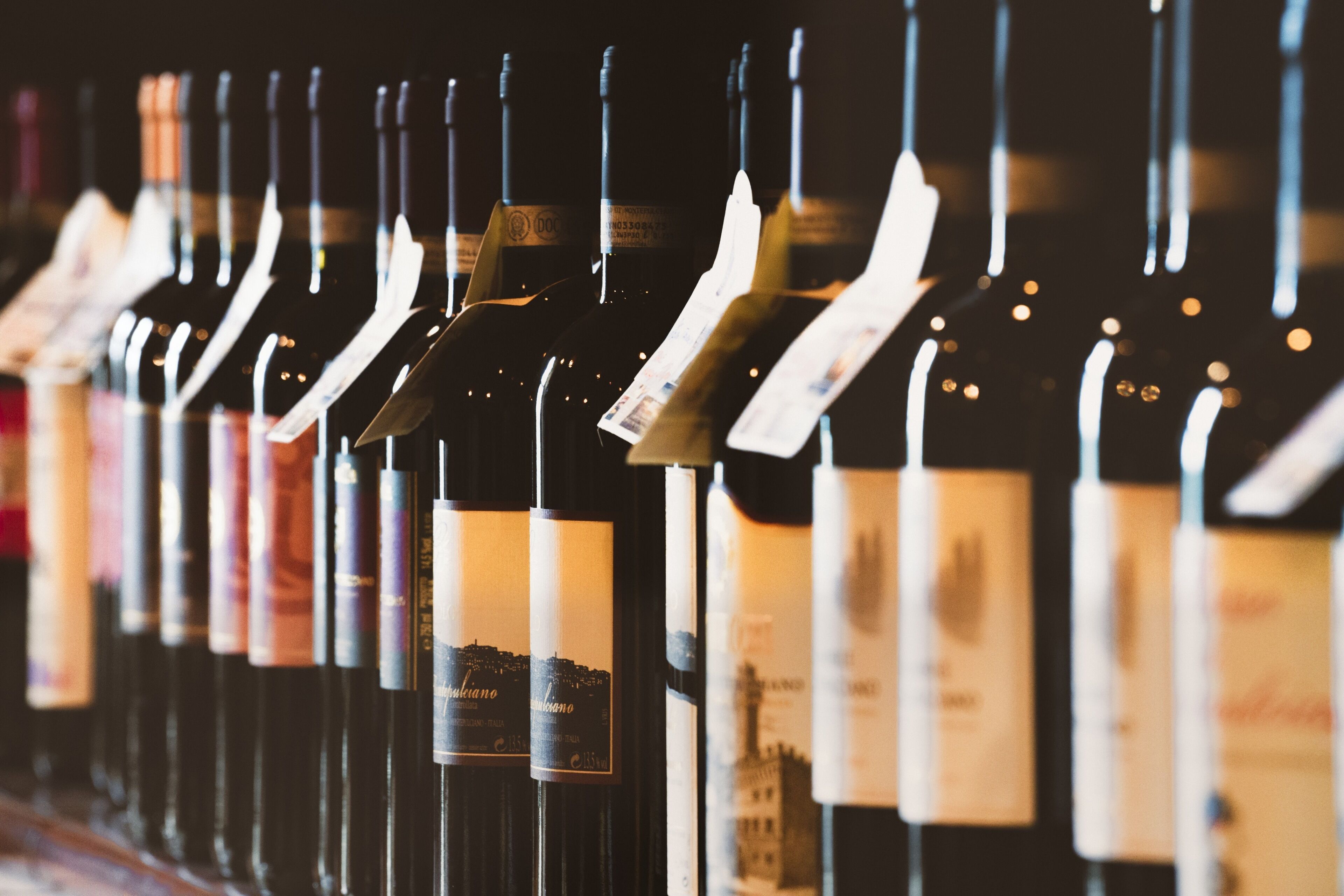A row of wine bottles with labels hanging from the necks, arranged in a neat line.