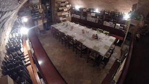 Una bodega con una larga mesa dispuesta para cenar, rodeada de botelleros y estanterías.