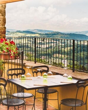 Una terraza con una mesa dispuesta para comer, sillas y una maceta con flores rojas.
