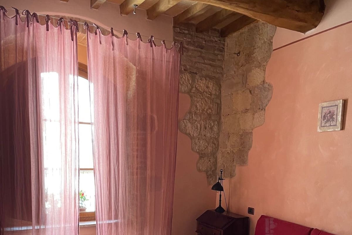 Un dormitorio con techo de madera, una cama con colcha estampada, una mesita de noche, una lámpara y una pared de piedra.