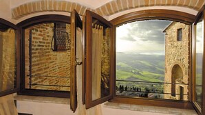 Una habitación con un amplio ventanal con vistas a un edificio de piedra y colinas ondulantes.