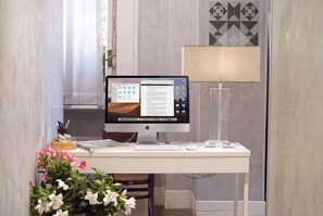 A desk with a computer, keyboard, mouse, and a lamp. There is a plant with flowers on the desk. - GHR Aventino Inn  (Rome)