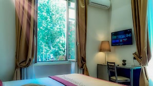 A hotel room with a bed, a desk, a chair, an air conditioning unit, a television, and a window with curtains. - Aventino Guest House (Rome)