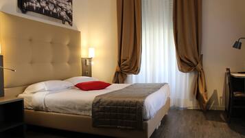 Ein Hotelzimmer mit Bett, Nachttisch, Lampe, einem Fenster mit Vorhängen und einem Wandbild.