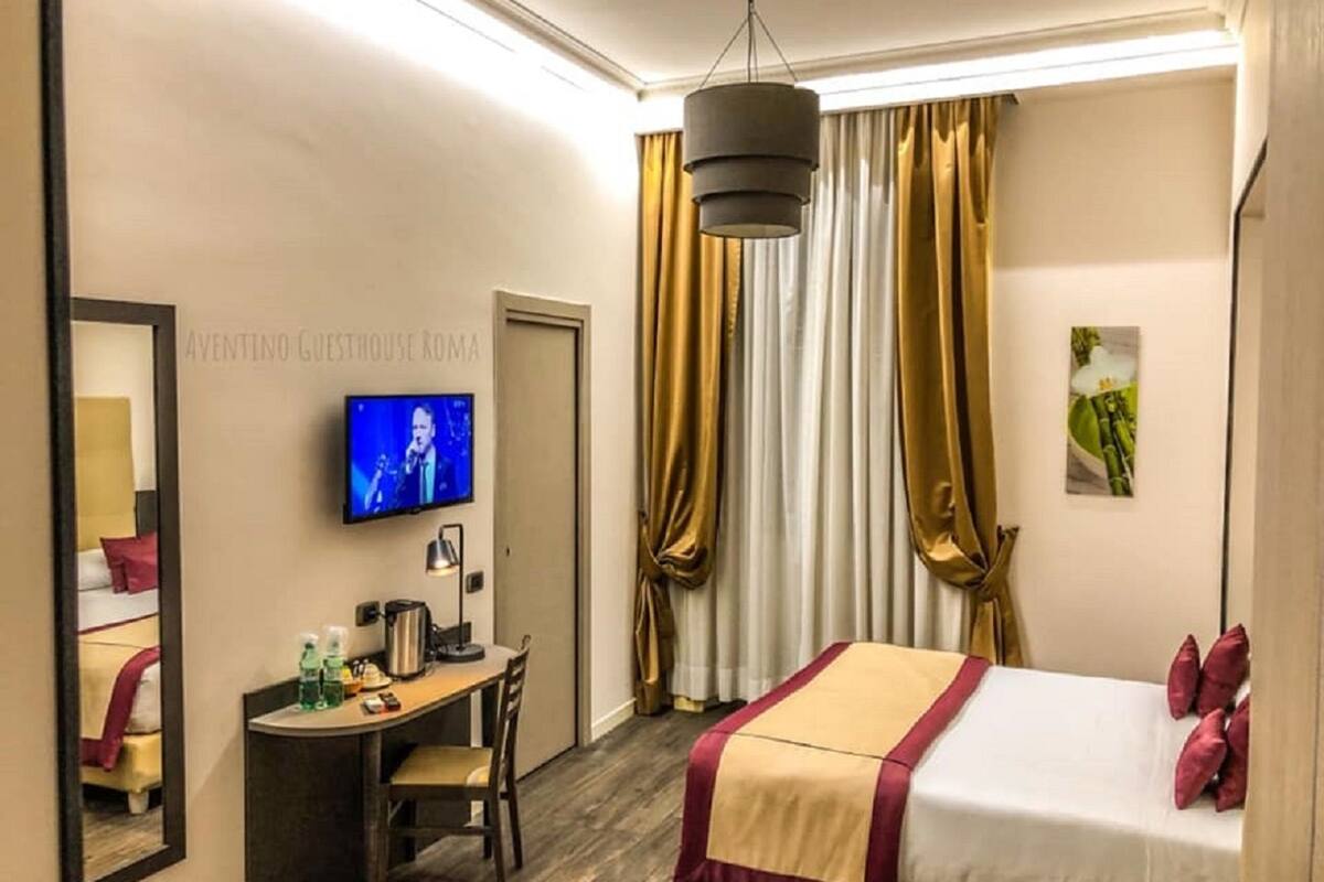 Una habitación de hotel con cama, escritorio, silla, televisor y espejo.