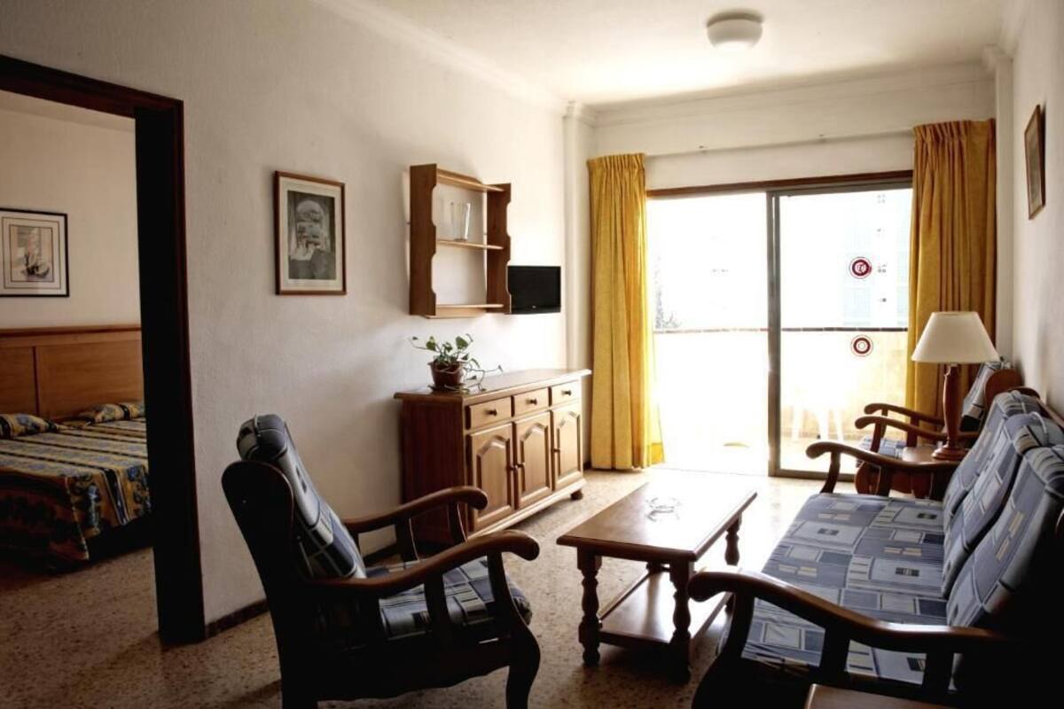 A room with a sofa, chairs, a wooden cabinet, a television, and a window with curtains.