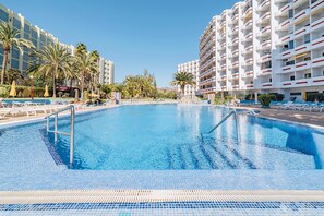 A swimming pool surrounded by palm trees and hotel buildings.