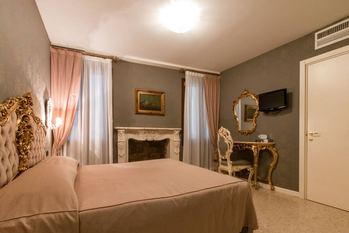 A bedroom with a large bed, a fireplace, a television, and a mirror on the wall.