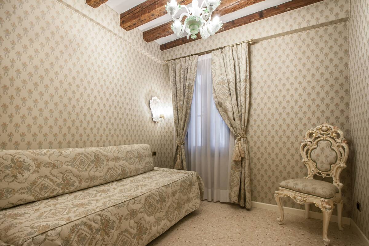 A room with patterned wallpaper, a sofa, a chair, and a window with curtains.