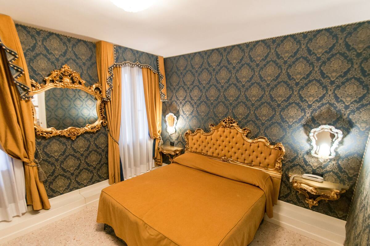 A bedroom with a large bed, ornate gold headboard, and a mirror with a gold frame.